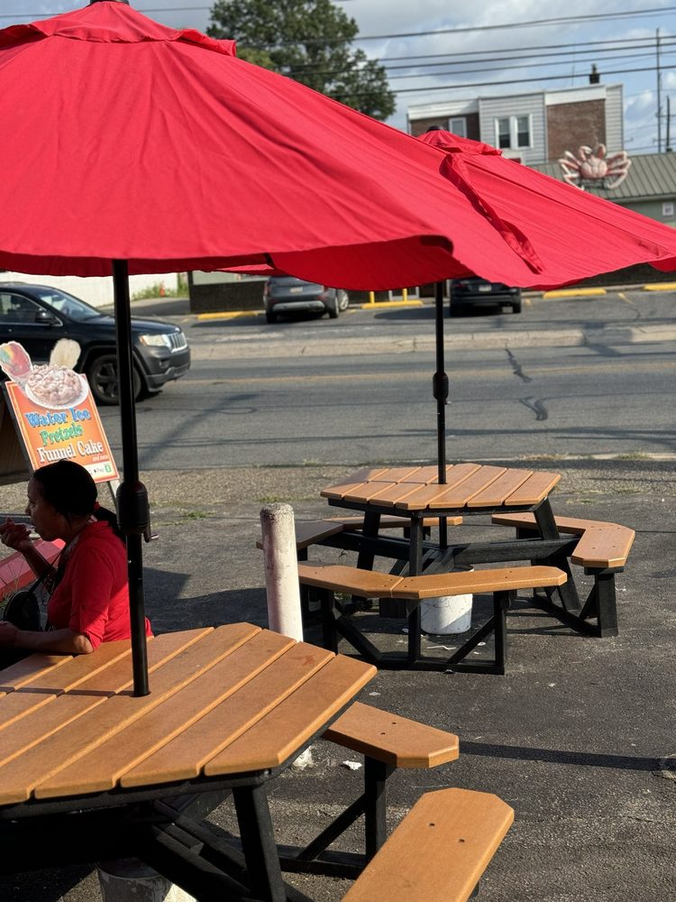 Outdoor picnic tables with red umbrellas near CJ's Waterice and Ice Cream.